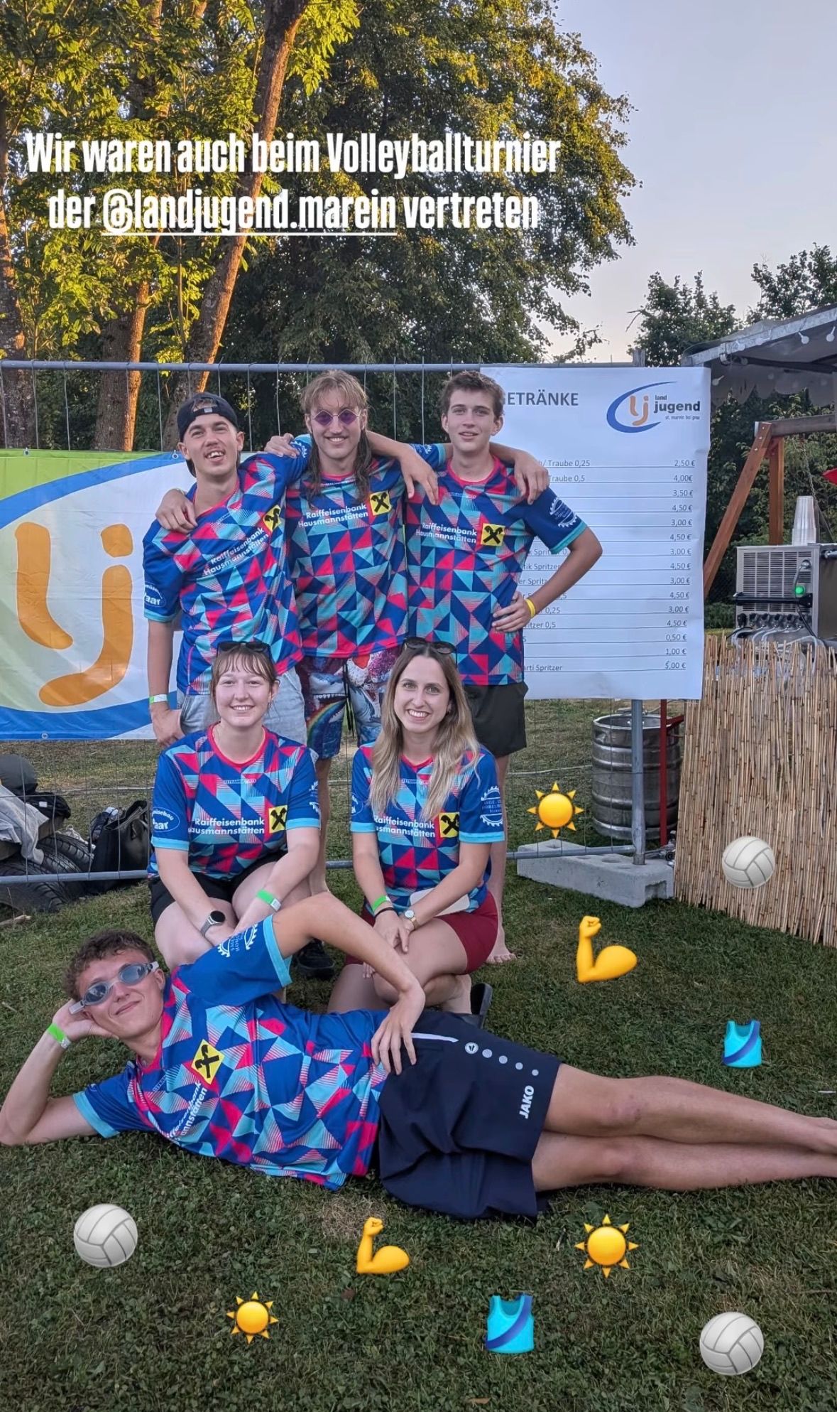 Eine Gruppe von fünf Personen in passenden blauen und pinkfarbenen Trikots posiert für ein Foto in einem Park. Sie stehen und sitzen auf dem Rasen mit einem weißen Brett und einem Banner im Hintergrund.