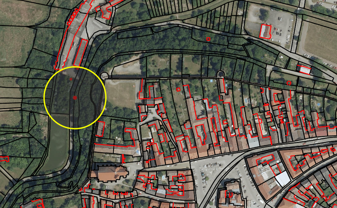 Luftbild zeigt ein Wohngebiet mit rot umrissenen Gebäuden. Ein gelber Kreis markiert einen bestimmten Ort. Grüne Bereiche und Bäume sind verstreut.