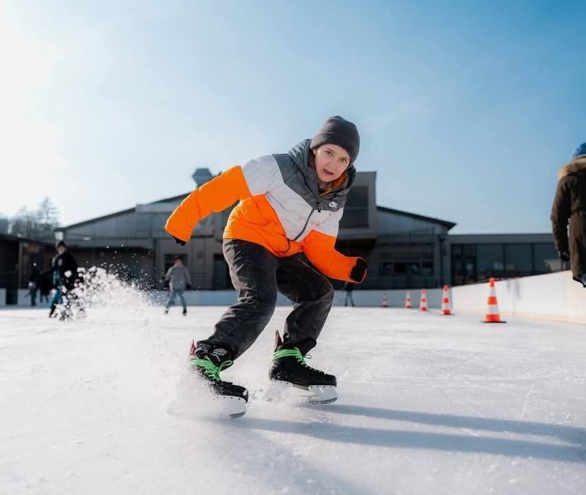 Eine Person  Eisskates auf einer Eisbahn mit Hütchen darum. Sie trägt ein Winteroutfit.