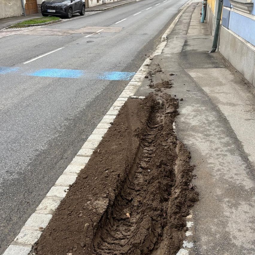 Ein Auto parkt am Straßenrand neben einem beschädigten Bordstein vor einem Gebäude.