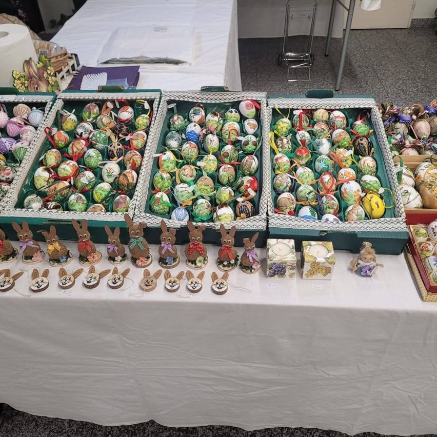 Ein Tisch zeigt verschiedene Osterdekorationen, darunter bemalte Eier und Figuren von Hasen. Der Tisch ist mit einem weißen Tuch bedeckt.