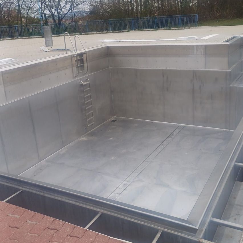 Ein leerer Edelstahlpool mit zwei Leitern an der Seite, umgeben von einem Betonzaun.