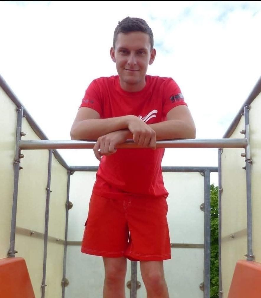 A man in red stands inside a metal structure, smiling and leaning on a railing.