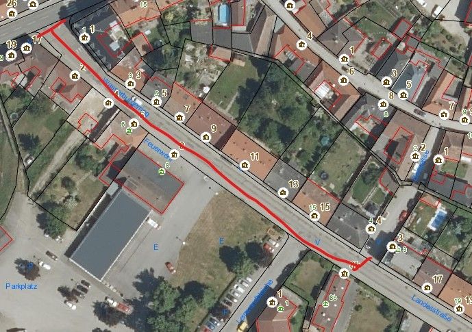 Aerial view of a neighborhood with labeled buildings and a red line indicating a road. Parking is marked on the left.