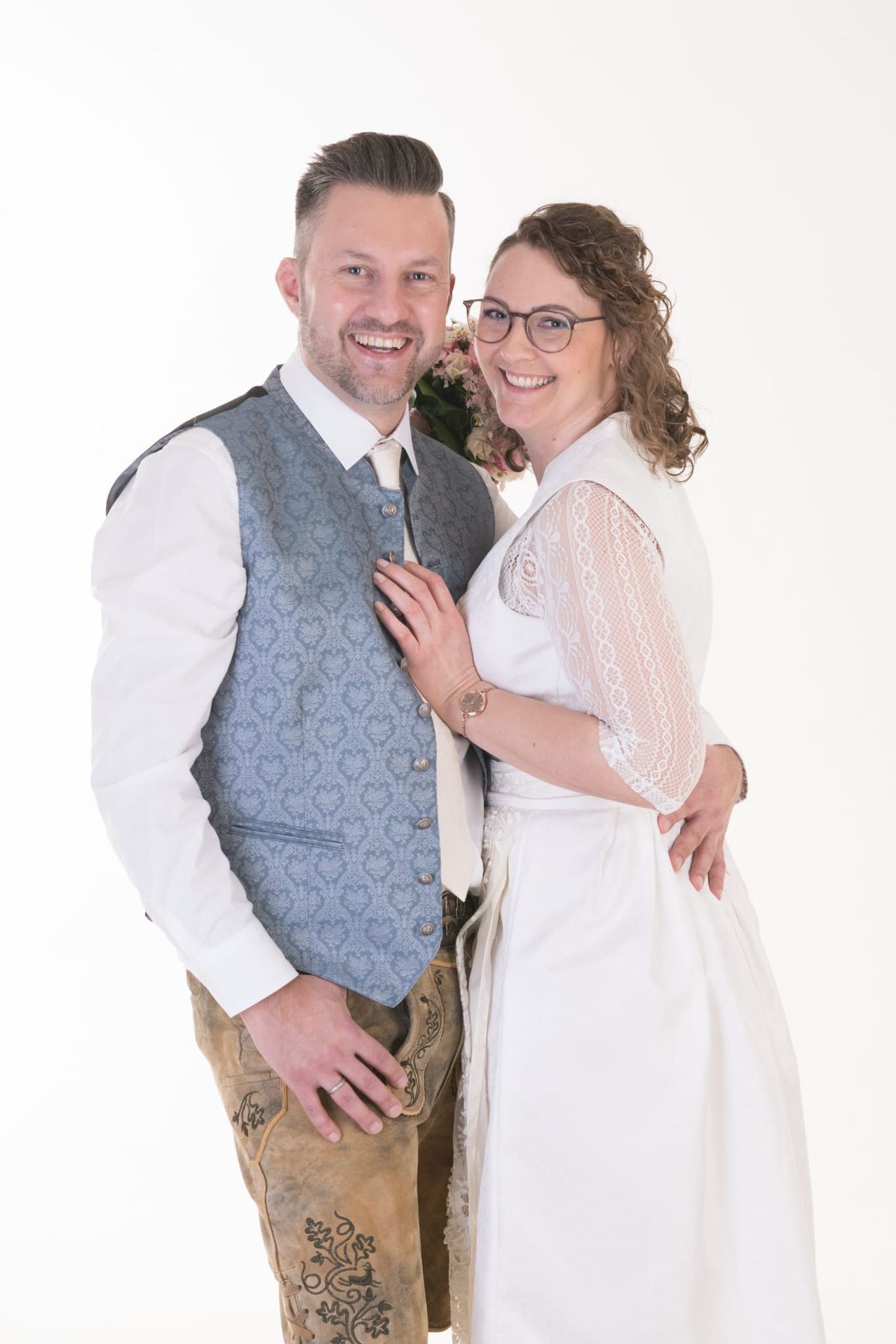 Ein Paar in traditioneller Kleidung, der Mann in einer Weste und die Frau in einem weißen Kleid, posiert zusammen.