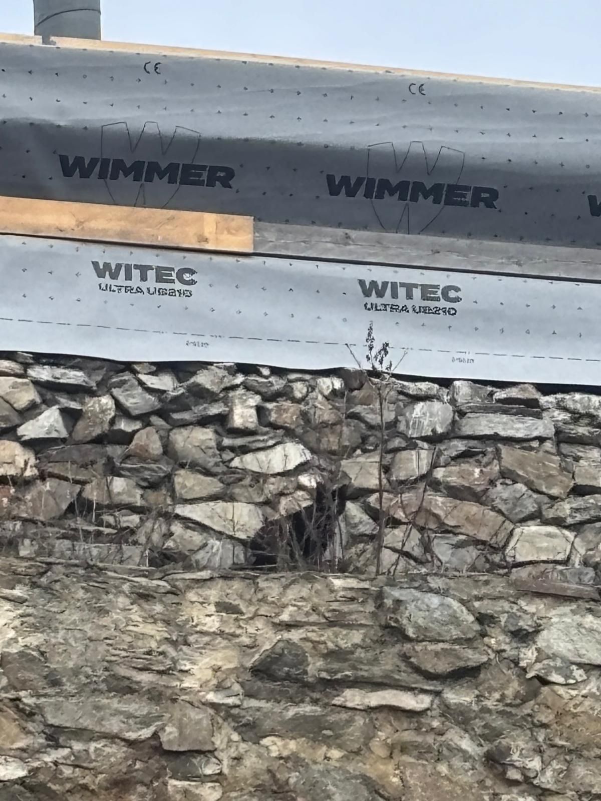 Eine Nahaufnahme einer Steinmauer mit einer grauen wasserdichten Membran, die mit 'WIMMER' und 'WITEC ULTRA UBZ20' beschriftet ist.