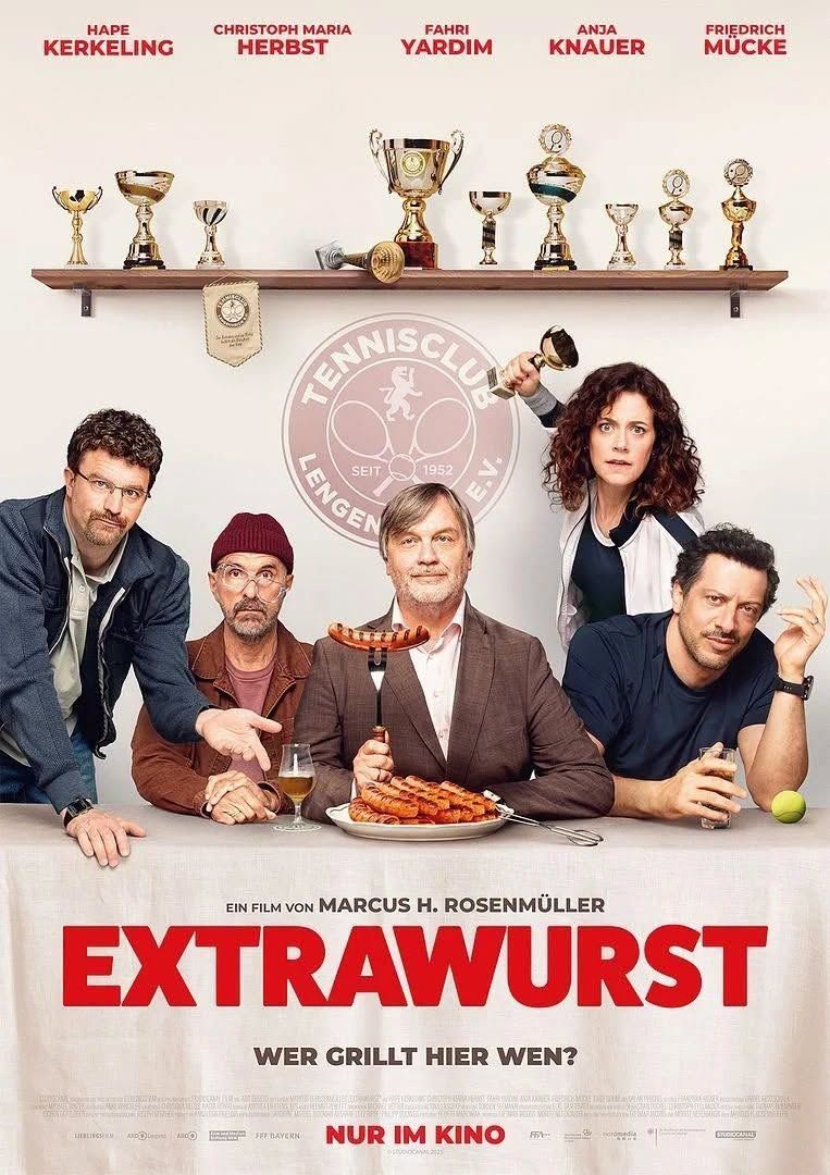 Filmplakat für den deutschen Film 'Extrawurst' mit einer Gruppe von Erwachsenen um einen Tisch mit einem Teller Würsten, ein Tennisclub-Logo über ihnen.