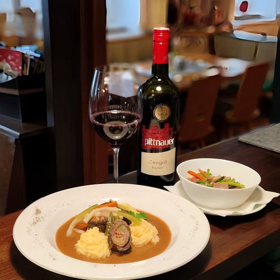 Ein Tisch mit einem Teller Fleisch und Gemüse, einer Schüssel mit gemischtem Gemüse und einer Flasche Wein.