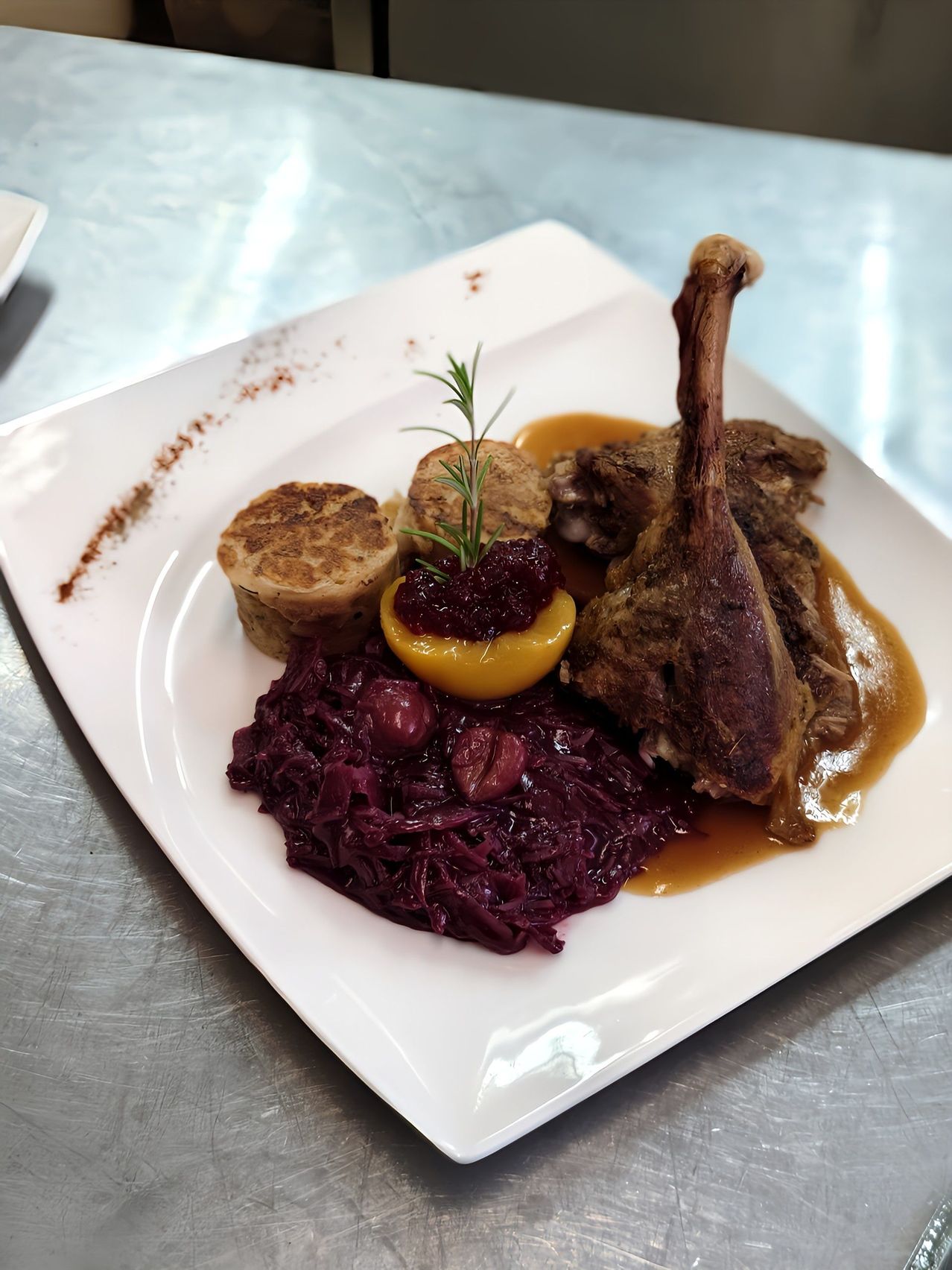 Ein weißer Teller mit einem Entenschenkel, Soße, Rotkohl und zwei Klößen, garniert mit einem Rosmarinzweig.