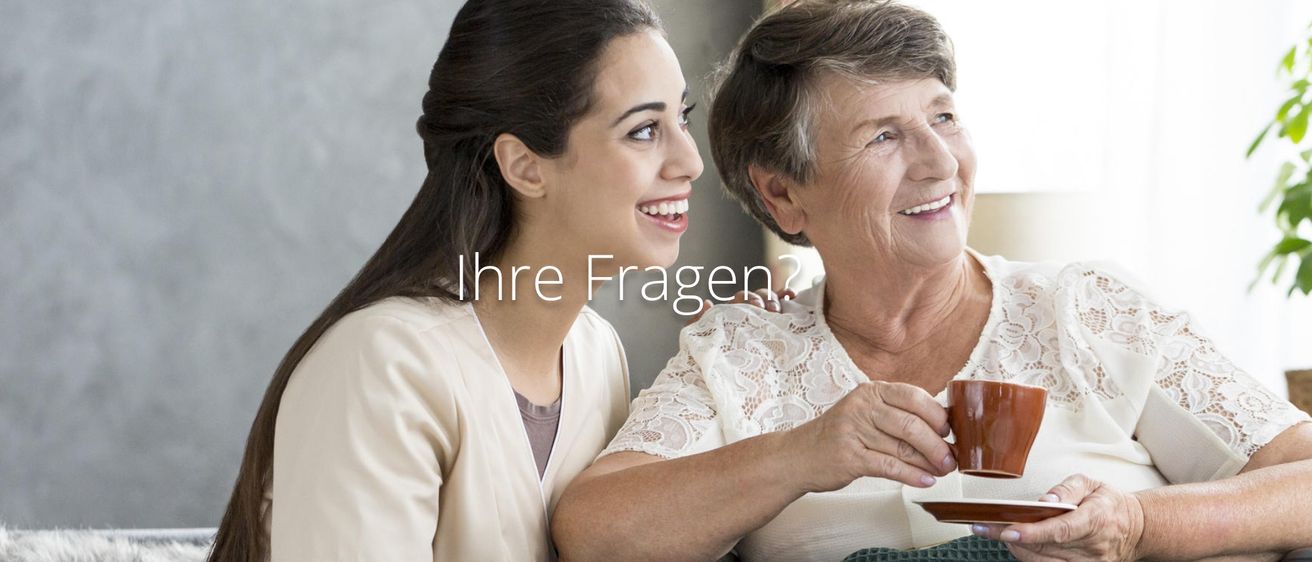 Eine lächelnde ältere Frau und eine junge Frau stehen nah beieinander und teilen einen Moment. Die ältere Frau hält eine Tasse. Der Text 'Ihre Fragen?' ist in Deutsch geschrieben.