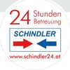 Rundes Aufkleber mit dem Text '24 Stunden Service SCHINDLER', mit roten und blauen Pfeilen, die aufeinander zeigen, und einem Website-Link www.schindler24.at.