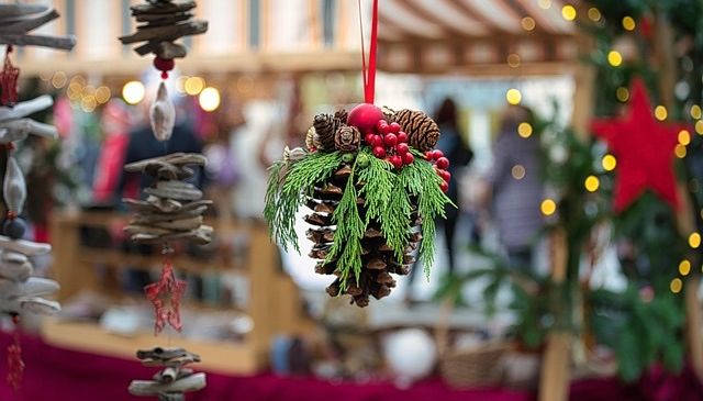Ein Weihnachtsmarkt-Display mit Tannenzapfen-Ornamenten, Lichterketten und einem roten Stern, im verschwommenen Hintergrund mit gehenden Menschen.
