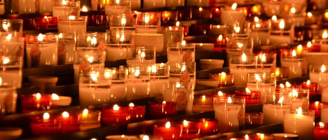 Eine große Sammlung von Kerzen in verschiedenen Farben und Größen ist in einem schwach beleuchteten Raum ausgestellt. Die Kerzen sind ordentlich in Reihen angeordnet.