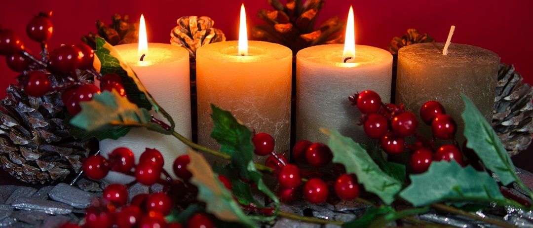Vier brennende Kerzen mit roten Beeren und grünen Blättern vor einem roten Hintergrund.