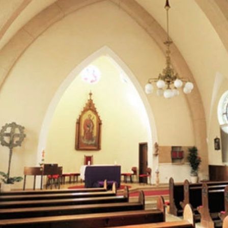 Ein Kircheninneres mit hohen Bögen, einer Laterne und einem geschmückten Altar mit einem Gemälde. Bänke sind zum Altar ausgerichtet, ein roter Teppich führt dazu.