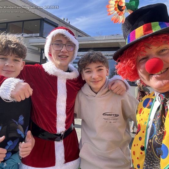 Vier Jungen, einer als Weihnachtsmann verkleidet, stehen zusammen vor einem Gebäude mit einem lächelnden Clown. Die Jungen lächeln und posieren für ein Foto.