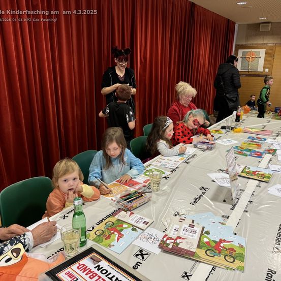 Eine Gruppe von Kindern und Erwachsenen sitzt um einen langen Tisch mit Büchern und Buntstiften herum. Eine Person steht hinter ihnen in der Nähe eines roten Vorhangs. Das Bild hat einen Wasserzeichen mit dem Datum 03/04/2025.