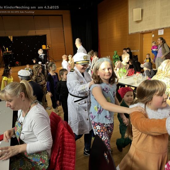 Am 4. März 2025 beim Kinderfasching tanzen mehrere Kinder in Kostümen in einem Saal, Erwachsene in Kostümen schauen zu, und andere sitzen an Tischen.