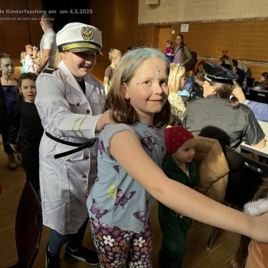 Ein junges Mädchen mit Gesichtsbemalung lächelt und posiert für ein Foto mit einer Frau in einer Marineuniform auf einem Kinderfasching am 4. März 2025.