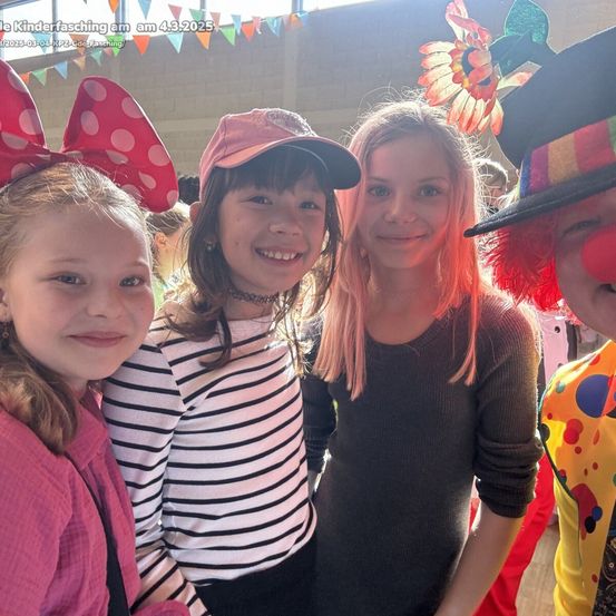 Vier Mädchen auf einer Kinderparty, eine mit einer Micky-Maus-Mütze, eine andere mit einer rosa Mütze, ein Clown im Hintergrund.
