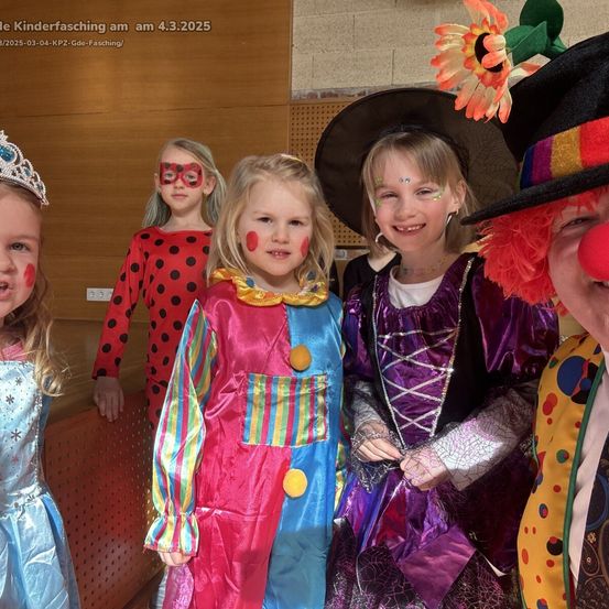 Fünf Kinder sind in bunten Kostümen für eine Feier gekleidet. Ein Kind trägt ein Clownskostüm, während ein anderes als Marienkäfer gekleidet ist. Sie alle lächeln und posieren für ein Foto.