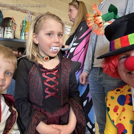 Eine Gruppe von Kindern in Kostümen, möglicherweise für eine Halloween-Party. Eine Mädchen mit Vampirzähnen steht in der Mitte.