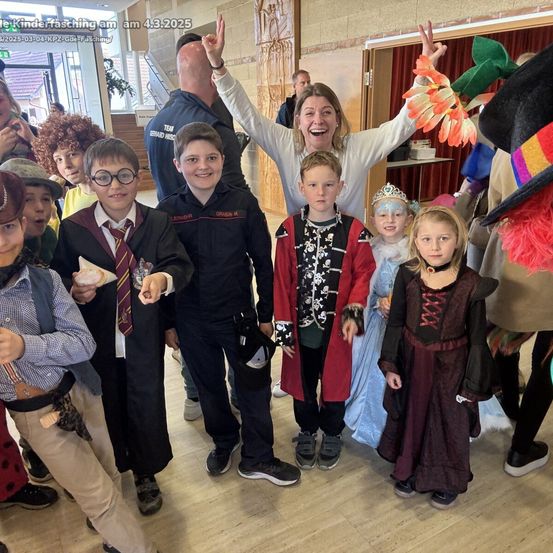 Eine Gruppe von Kindern in verschiedenen Kostümen, darunter Harry Potter und Hexen, posiert für ein Foto mit einer erwachsenen Frau und einem Mann bei einem Kinderfasching am 4. März 2025.