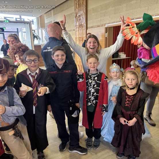 Kinder und Erwachsene in verschiedenen Kostümen, die für ein Foto beim Schulkarneval am 4. März 2025 posieren. Eine Frau und ein Polizist sind ebenfalls anwesend.