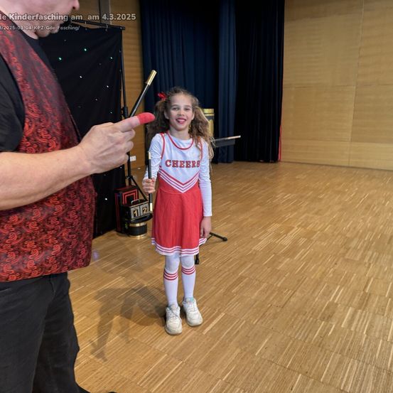 Ein Mann führt einen Zaubertrick für ein junges Mädchen in einer Cheerleader-Uniform auf einer Bühne vor. Das Bild ist vom 3. März 2025.