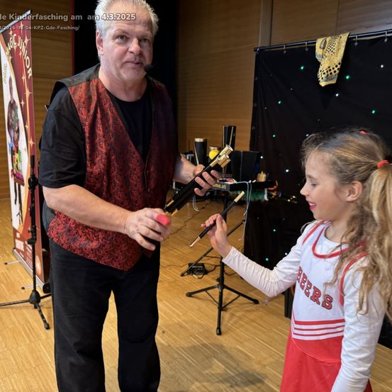 Ein Zauberer zeigt einer kleinen Cheerleaderin einen Trick vor einem schwarzen Hintergrund.