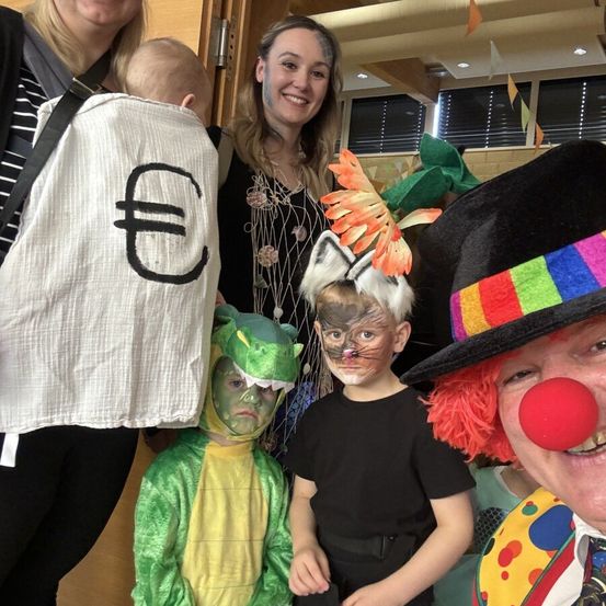 Eine Gruppe von Menschen in Kostümen, darunter ein Clown, eine Katze, ein Dinosaurier und ein Euro-Taschen, posiert für ein Foto.