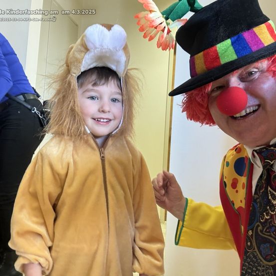 Ein Kind in einem Löwenkostüm und ein Clown in einem bunten Hut, lächelnd, auf der Bühne.