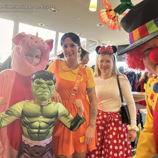 Eine Gruppe von Menschen in Kostümen bei einem Kinderkarneval, einer als Schwein, einer als Clown und einer als Mädchen verkleidet.