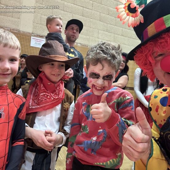 Eine Gruppe von Kindern in verschiedenen Kostümen bei einer Veranstaltung. Ein Clown, ein Junge im Cowboy-Outfit, ein Junge mit dinosaurier-thematischer Kleidung und ein Junge im Spider-Man-Kostüm.