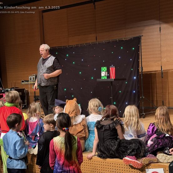 Ein Mann führt eine Zaubershow auf der Bühne vor einer Gruppe von Kindern in Kostümen auf.