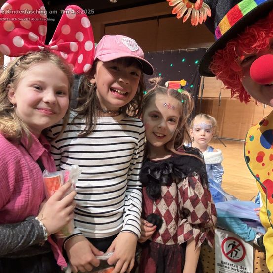 Vier Mädchen und ein Clown lächeln für ein Foto. Drei Mädchen haben Gesichtsbemalung, und eine trägt eine Mütze. Sie sind auf einer Kinderparty, mit einem Schild, das 'Betreten verboten' sagt.