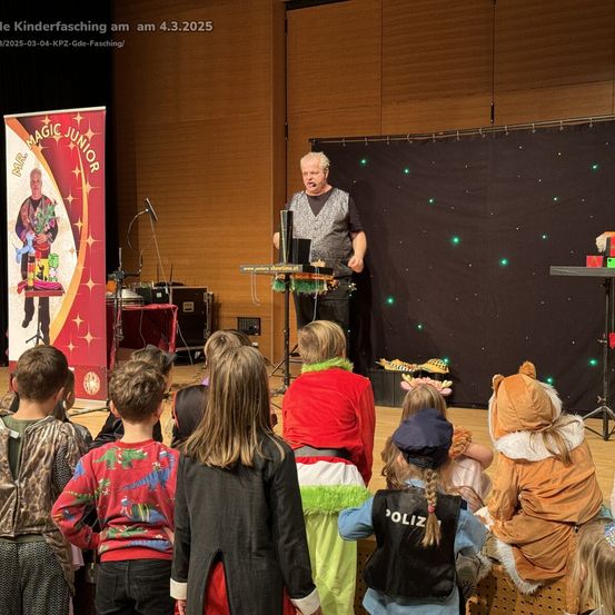 Ein Zauberer namens Mr. Magic Junior tritt auf der Bühne für eine Gruppe von Kindern in Kostümen auf. Das Publikum beobachtet ihn.