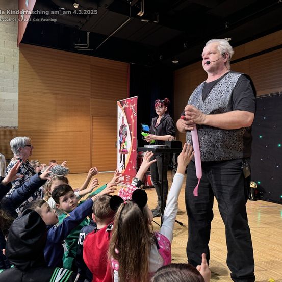 Ein Zauberer unterhält Kinder auf einem Kinderfasching am 4. März 2025. Er hält einen rosa Luftballon, während Kinder begeistert die Hände heben.