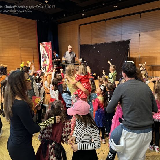 Kinderfasching am 4.3.2025. Erwachsene und Kinder in Kostümen versammeln sich für eine Aufführung, mit einem Zauberer auf der Bühne und anderen Zuschauern.