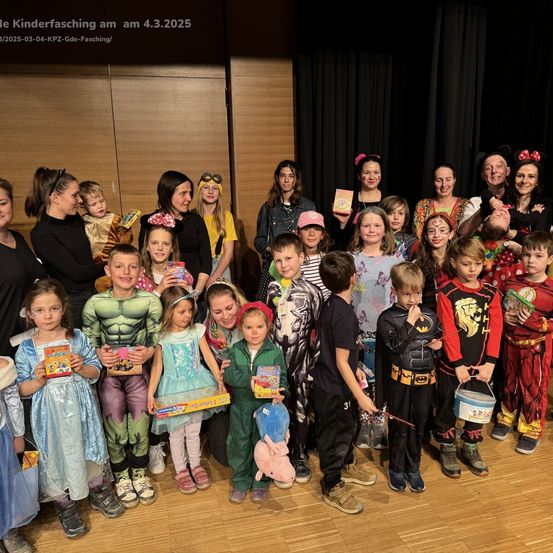 Eine Gruppe von Kindern und Erwachsenen in Kostümen posiert für ein Foto auf einer Bühne. Einige halten Geschenke, und ein Datumsstempel zeigt den 4.3.2025.