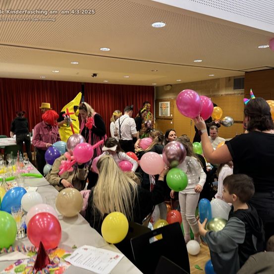 Eine Gruppe von Menschen in einem mit Luftballons gefüllten Raum, wahrscheinlich bei einer Kinderparty am 4. März 2025. Die Leute halten Luftballons und einige tragen Kostüme.