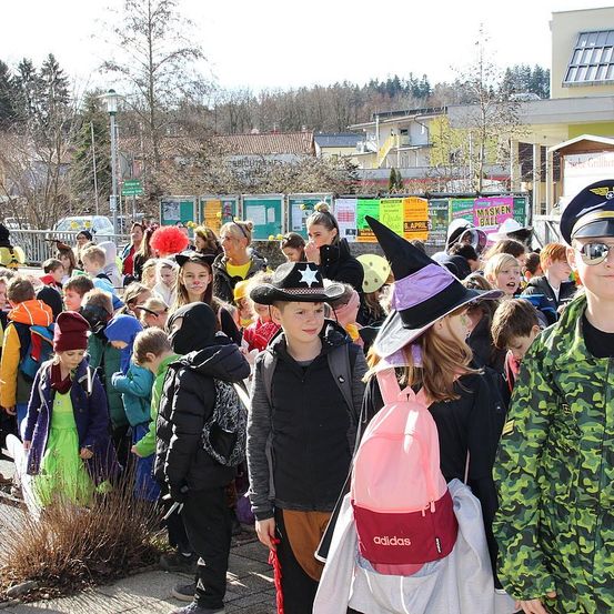 Eine große Gruppe von Kindern in Kostümen und Hüten, möglicherweise für eine Halloween-Veranstaltung, stehen draußen vor einem Gebäude.