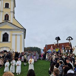Eine religiöse Prozession vor einer Kirche mit Teilnehmern in traditionellen Kostümen. Die Kirche hat einen hohen Turm und komplizierte Designs.