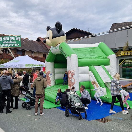 Eine Menschenmenge versammelt sich um ein aufblasbares Mickey-Mouse-Bounce-Haus, einige Kinder spielen und andere beobachten.