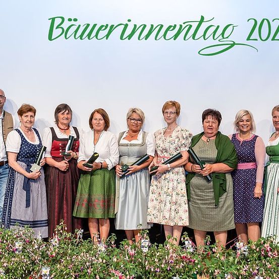 Eine Gruppe von Menschen in traditioneller Kleidung steht zusammen und hält Auszeichnungen. Sie stehen vor einem Banner mit der Aufschrift 'Bauerninnentag 2023'. Sie lächeln und posieren für ein Foto.
