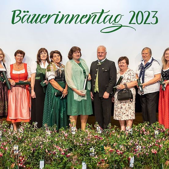 Eine Gruppe von Erwachsenen in traditioneller bayerischer Kleidung steht gemeinsam beim Bayerischen Inn Tag 2023 Event. Sie halten Auszeichnungen und posieren für ein Foto.