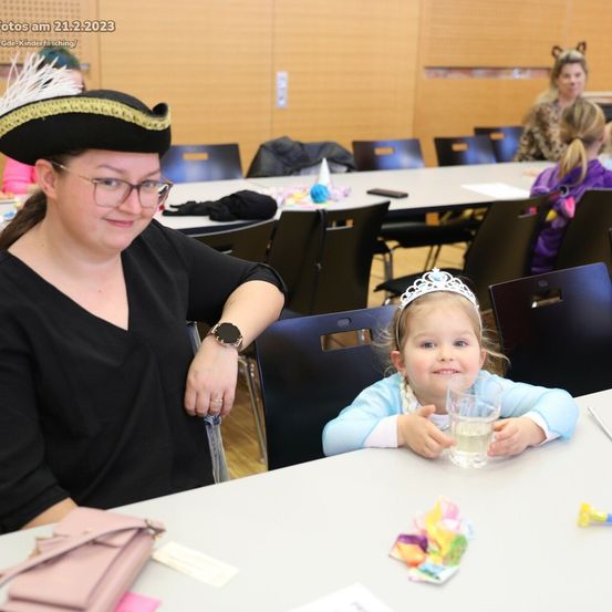 Eine Frau mit einem Piratenhut sitzt neben einem kleinen Mädchen mit Krone, das ein Glas hält, an einem Tisch in einem Raum mit anderen Tischen und Stühlen. Datumsangabe oben links.
