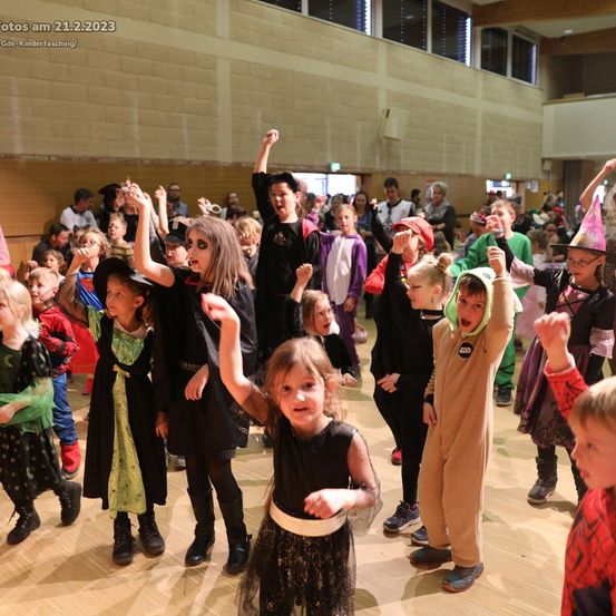Eine Gruppe von Kindern in verschiedenen Kostümen führt einen Tanz in einer Halle auf. Das Bild hat einen Wasserzeichen mit dem Datum '21.2.2023' oben links.