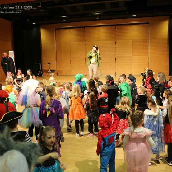 Eine Gruppe von Kindern in Kostümen auf einer Bühne, ein Mann in einem grünen Kostüm führt in der Mitte auf. Verschiedene andere Charaktere und Erwachsene sind anwesend. Das Bild wurde am 21. Februar 2023 aufgenommen.