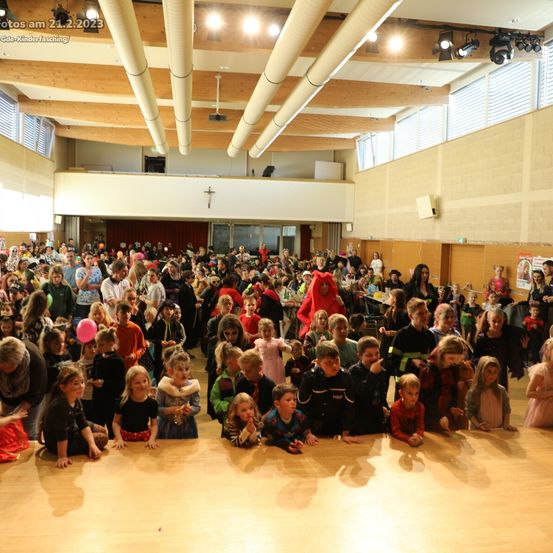 Ein Saal mit Holzböden und einer Holzdecke, eine große Gruppe von Kindern in Kostümen posiert für ein Foto. Das Bild wurde am 21. Februar 2023 aufgenommen.